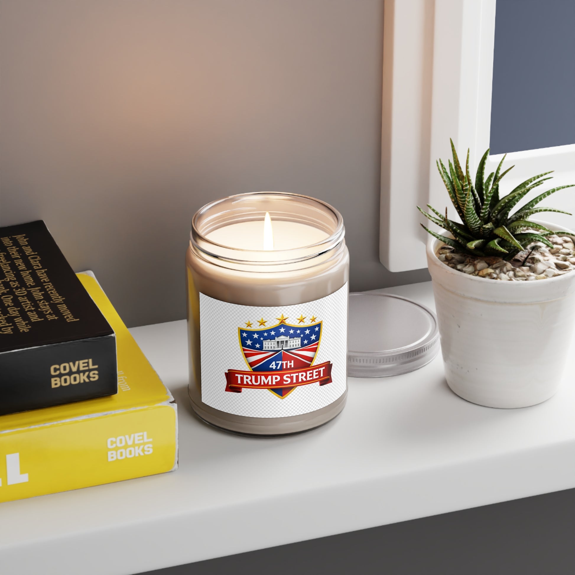 Candle in a glass jar with a 'Trump Street' label on a shelf with books and a plant.